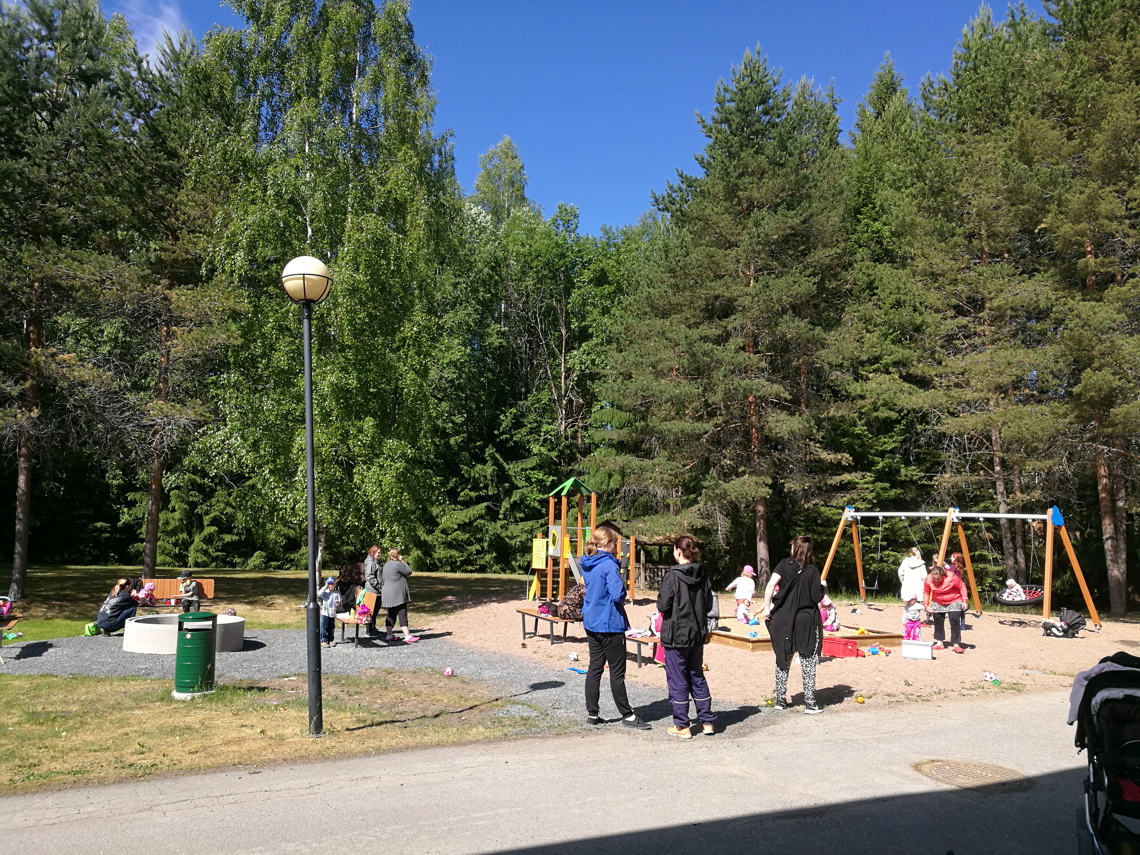 Perhekerhon puuhaviikko Leikkipuistossa ihmisiä seisomassa ja lapsia keinumassa.