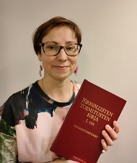 Minna-pappi kuvassa kirkollisten toimitusten kirjan kanssa iloisesti hymyilevänä.