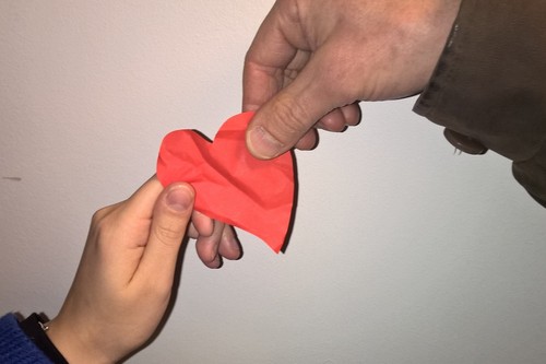 Kuva, jossa kahden henkilön kädet pitävät kiinni punaisesta paperisydämestä
